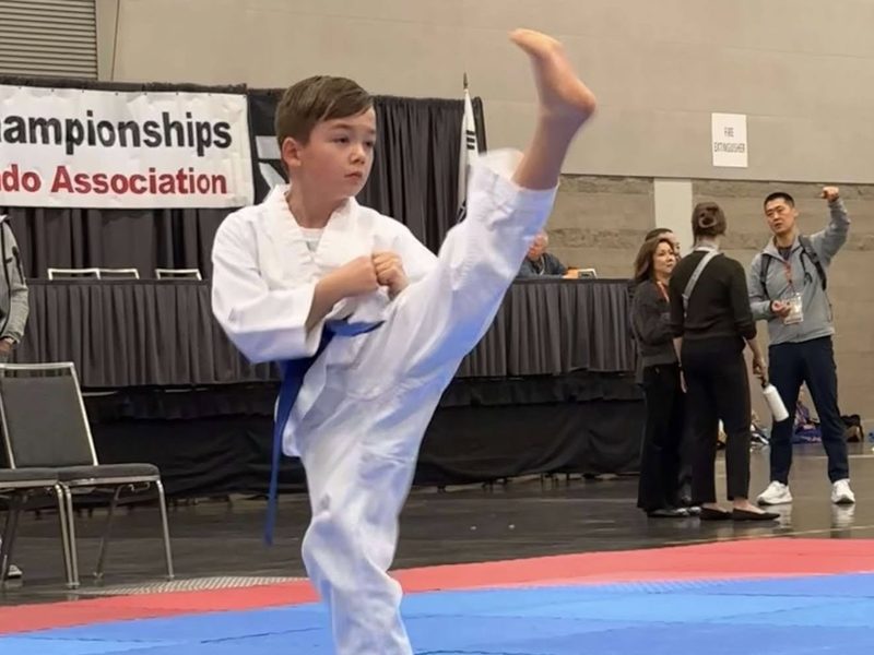 A blue-belt student landing a high kick in competition.