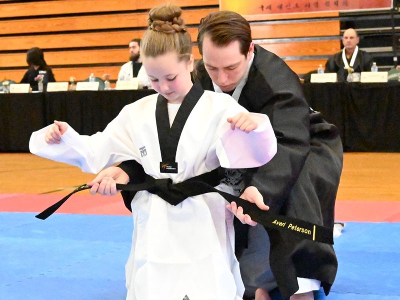 A student receiving her black belt from an instructor at a promotion ceremony.