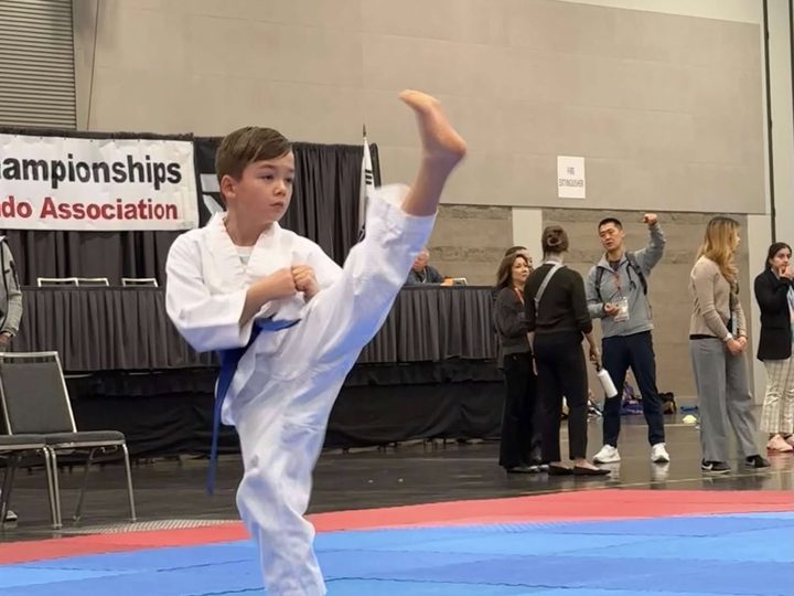 A blue-belt student throwing a high kick during a tournament match.