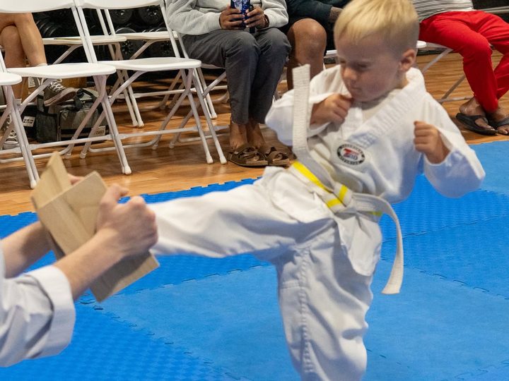 A young Lil' Dragons student in a white dobok and yellow belt striking a hand target.