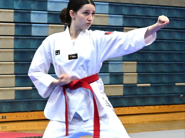 A red-belt teen student holding a forward stance mid-form.